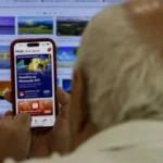 Imagem mostra idoso usando celular em frente a tela do computador