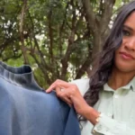 Uma mulher de cabelos longos e roupa clara segura uma blusa de frio azul desgastada.