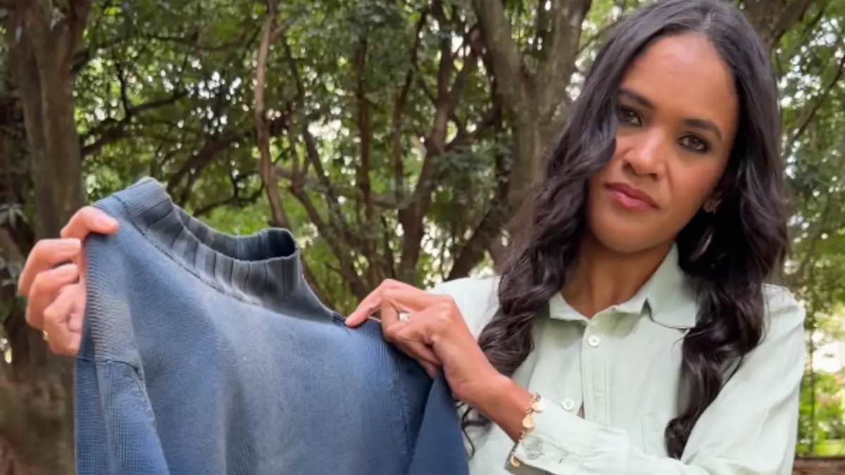 Uma mulher de cabelos longos e roupa clara segura uma blusa de frio azul desgastada.